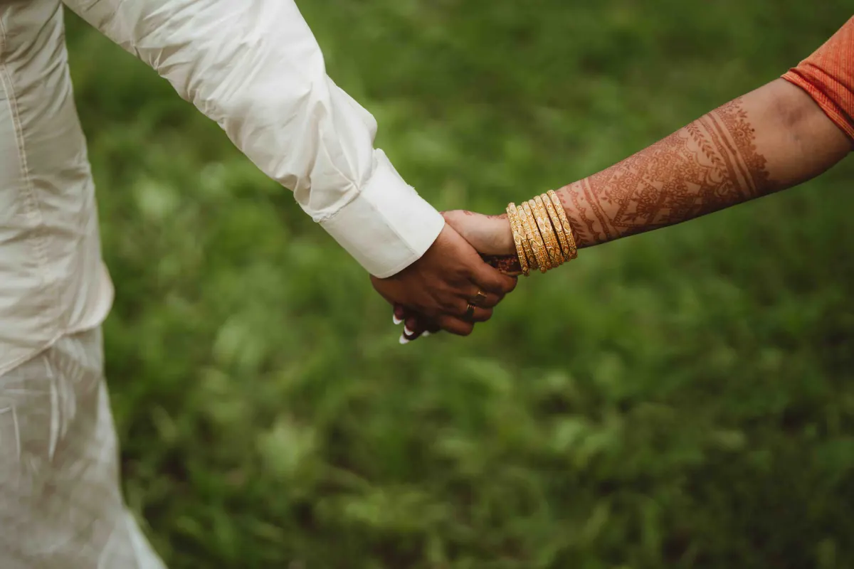 Two hands clasped, one wearing gold bangles